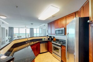 A modern kitchen with a large island, stainless steel appliances, and wooden cabinets. - Expansive Beachfront Condo at Waterscape w a Shared Pool, Hot Tub, & Lazy River (Fort Walton Beach)
