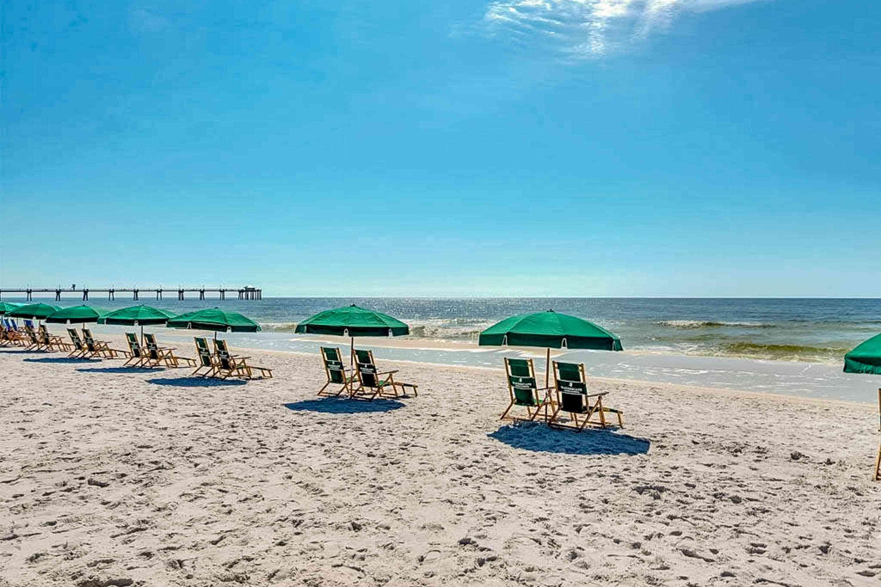 A beach with rows of green umbrellas and lounge chairs.