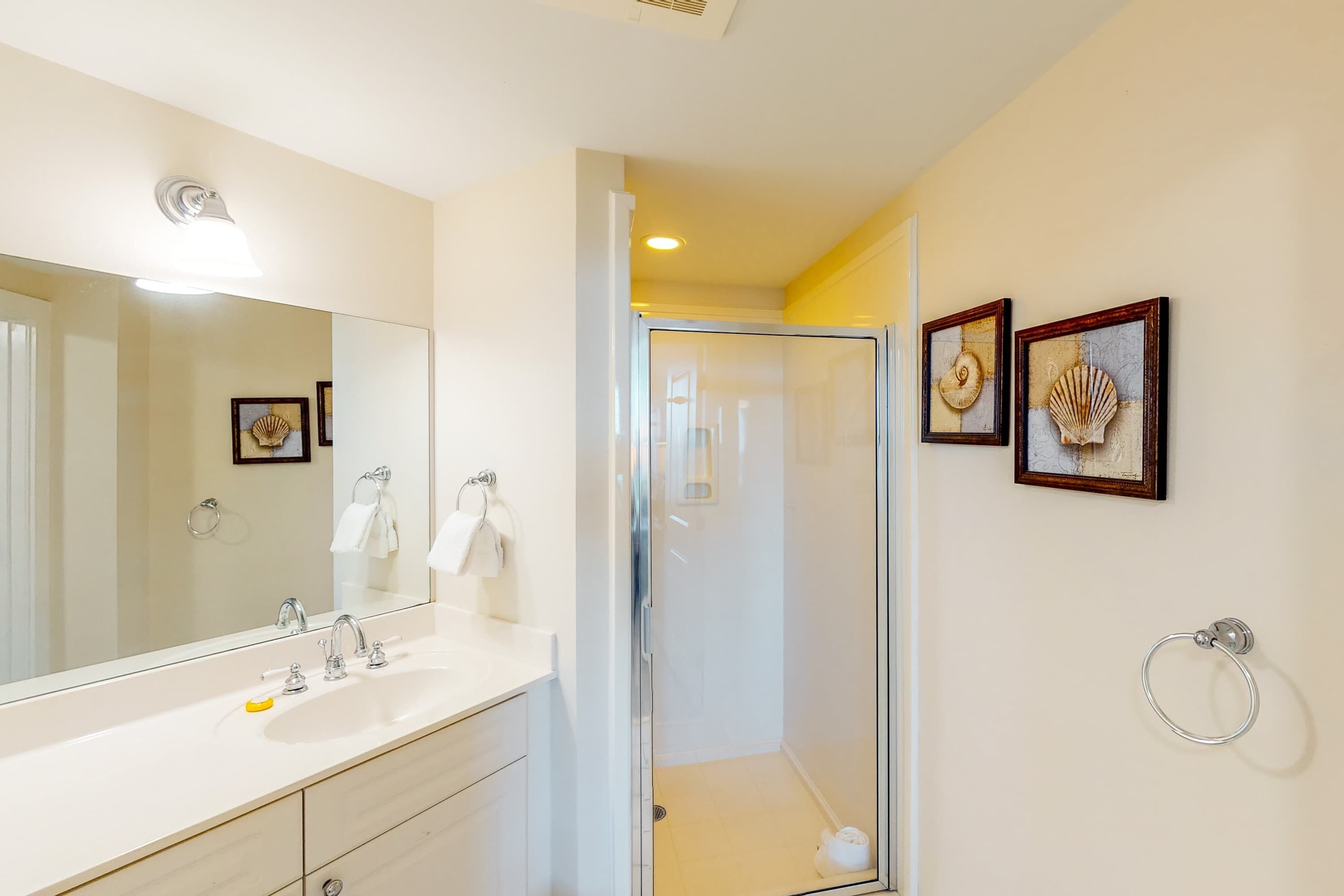 Une salle de bain avec un grand miroir, un espace douche et deux coquillages encadrés accrochés au mur.