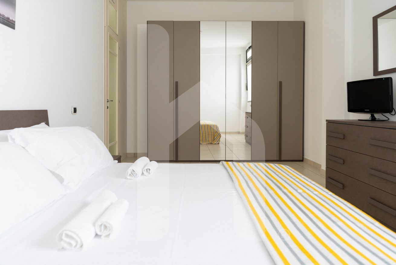 Een hotelkamer met een bed, een kledingkast, een televisie en een badkamer zichtbaar achter een deur.