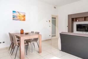 A modern living room with a wooden dining table, chairs, a flat-screen TV, and a painting of a sunset. - Homiday - Maximum's Landing (Roseto degli Abruzzi)