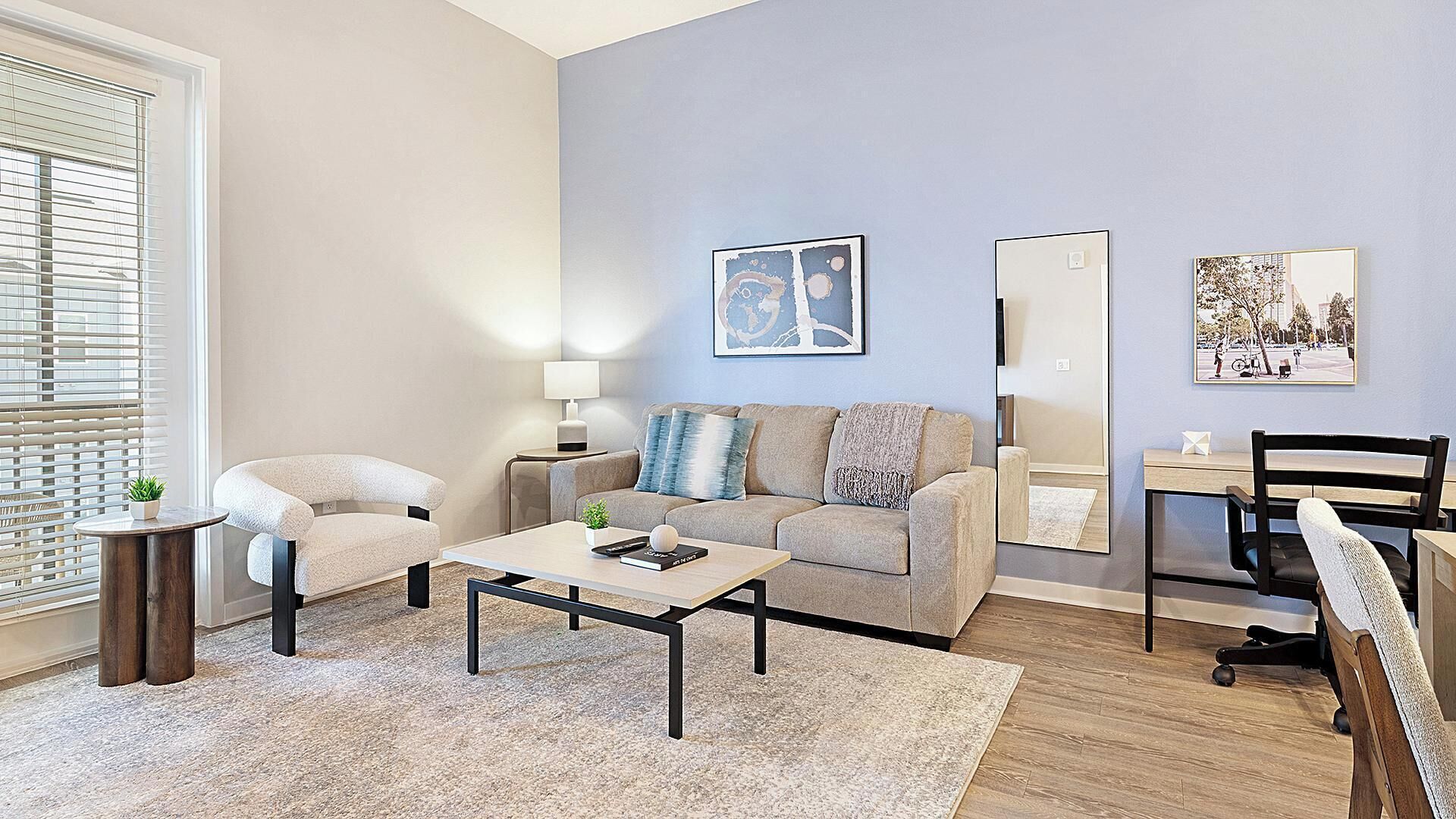 A modern living room with a sofa, two armchairs, a coffee table, a side table with a lamp, and a large mirror.