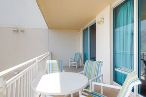 Ein Balkon mit einem weißen Tisch, gestreiften Stühlen, einer Schiebetür aus Glas und einem weißen Geländer.