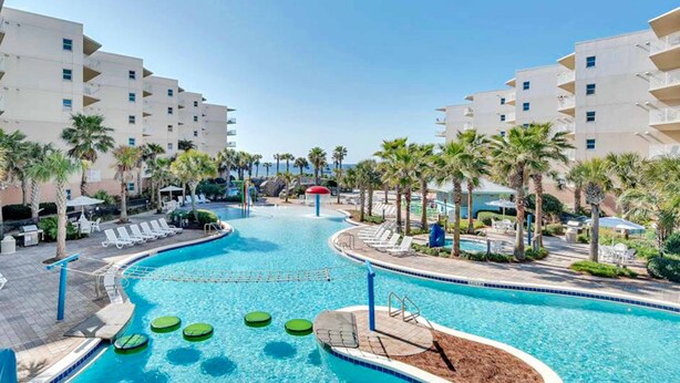A swimming pool area with lounge chairs and palm trees. - 5th Floor Gulf-Front Condo w Free WiFi, Shared Hot Tub, Outdoor Pool, & More (Fort Walton Beach)