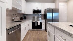 Una cocina moderna con armarios blancos, electrodomésticos de acero inoxidable y una encimera de granito.