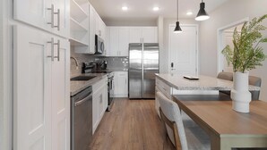 Une cuisine moderne avec des meubles blancs, des appareils électroménagers en acier inoxydable et un coin repas en bois.