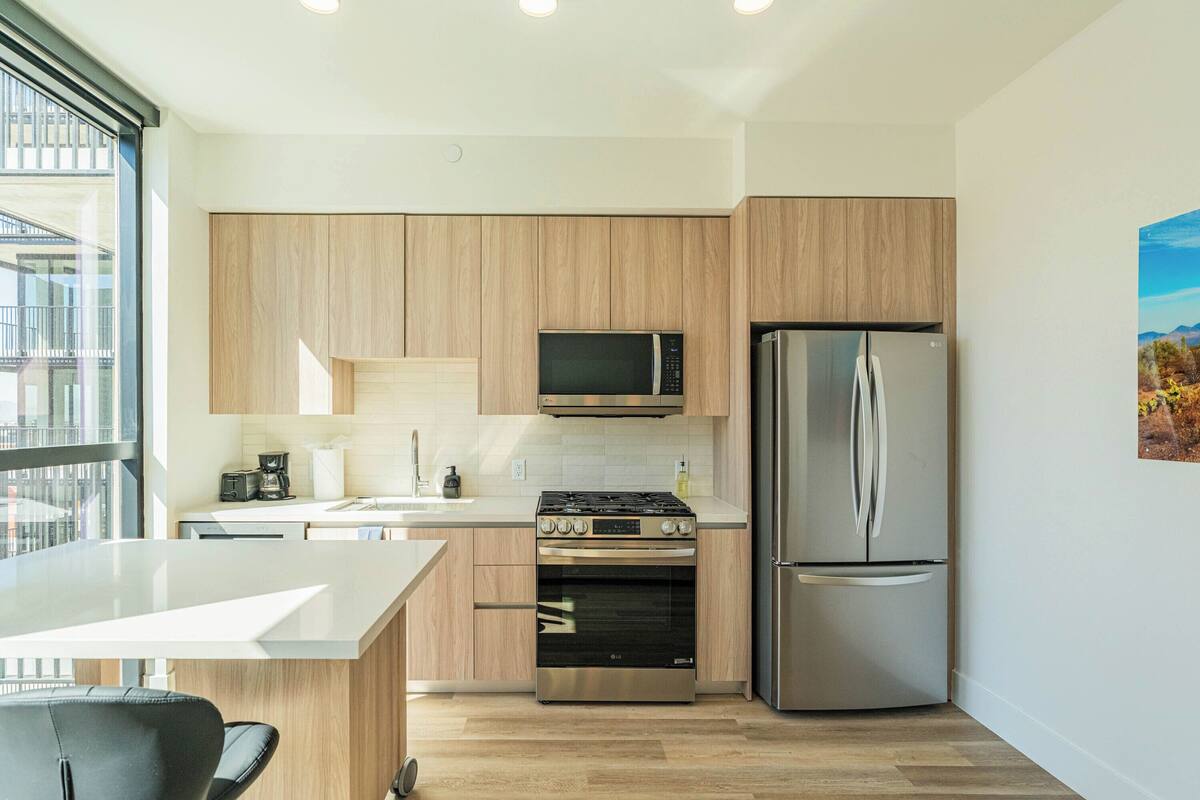Een moderne keuken met houten kastjes, roestvrijstalen apparatuur, een inbouwoven en een groot raam met uitzicht op de stad.
