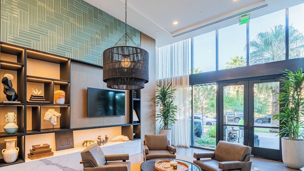 Un vestíbulo moderno con televisor, asientos cómodos, una planta grande en maceta y vistas al exterior.