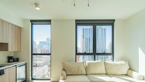 Un apartamento moderno con cocina, un sofá color beige y ventanas amplias con vistas a la ciudad.