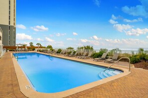 A rectangular swimming pool with a tiled edge, surrounded by lounge chairs and a brick patio. - Beautiful condo, balcony, sauna & pool access (Panama City Beach)