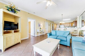 A living room with a television, a sofa, a coffee table, and a ceiling fan. - Beautiful condo, balcony, sauna & pool access (Panama City Beach)