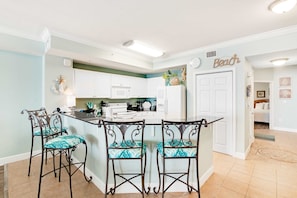 A kitchen with a central island, white cabinets, and a 'Beach' sign on the wall. - Gulf & Oceanfront Condo w/Shared In/Outdoor Pools, Hot Tub, High-Speed WiFi (Panama City Beach)