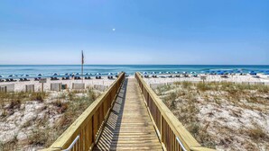 A wooden boardwalk leading to a beach with blue umbrellas and lounge chairs. - Gorgeous, cozy beachfront condo with pool, pool spa & beach access (Perdido Key)