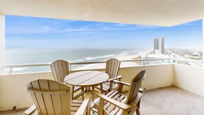 Un balcone con tavolo e sedie, affacciato su una spiaggia e un edificio alto.
