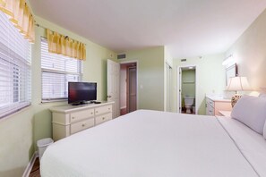 Een slaapkamer met een bed, een televisie op een dressoir, een badkamer met toilet en wastafel, en een deur die naar een andere kamer leidt.