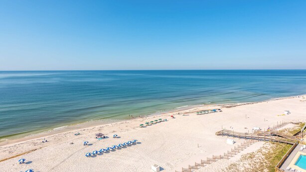 Una spiaggia con file di ombrelloni, una passerella in legno e una zona piscina.
