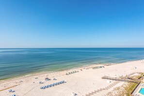 A beach with rows of umbrellas, a wooden walkway, and a pool area. - Top-Floor, Gulf-Front Condo w/ Balcony, Beach Access & Shared Pools/Hot Tub/Gym (Perdido Key)