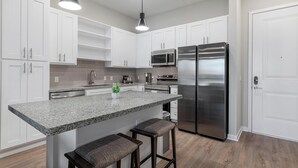 Una cocina moderna con armarios blancos, encimera de granito, electrodomésticos de acero inoxidable y una zona con taburetes de bar.