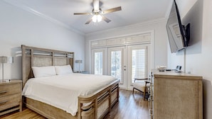 Ein Schlafzimmer mit einem hölzernen Bett, einem Nachttisch, einem Schreibtisch, einem Stuhl, einem Kleiderschrank, einem Deckenventilator und einem an der Wand befestigten Fernseher.