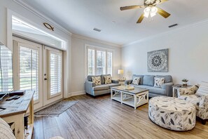 A spacious living room with a wooden floor, two grey sofas with patterned cushions, a coffee table, a ceiling fan, and a large window with blinds. - Enchanting home with pool, tennis, golf and washer/dryer (Miramar Beach)