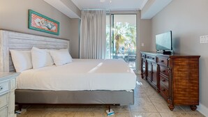 Quarto com cama, cómoda de madeira, televisão e ventoinha no teto.