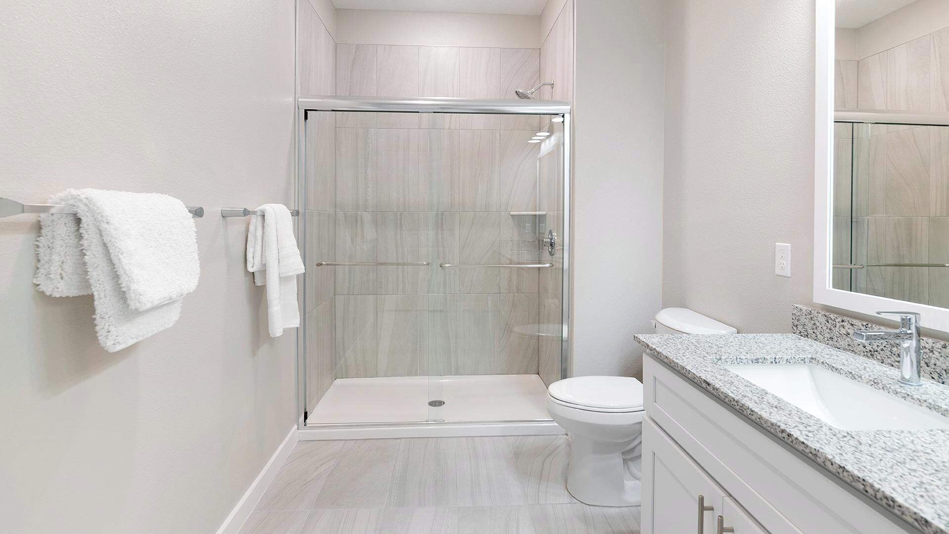 A modern bathroom with a glass-enclosed shower, a toilet, and a granite countertop with a sink.