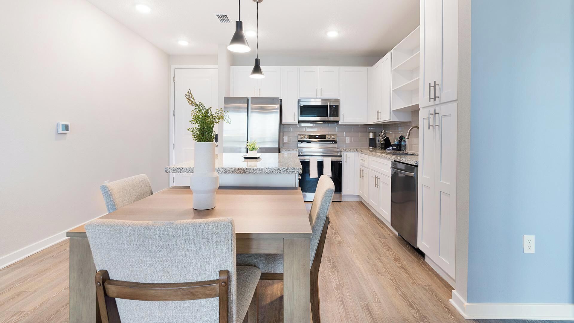 A modern kitchen with white cabinets, stainless steel appliances, and a wooden dining table with chairs.