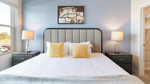 A neatly made bed with white and yellow pillows, a grey headboard, and two bedside tables with lamps. - Landing | Spectacular 2BD, Yoga Studio, Gym (Four Corners)