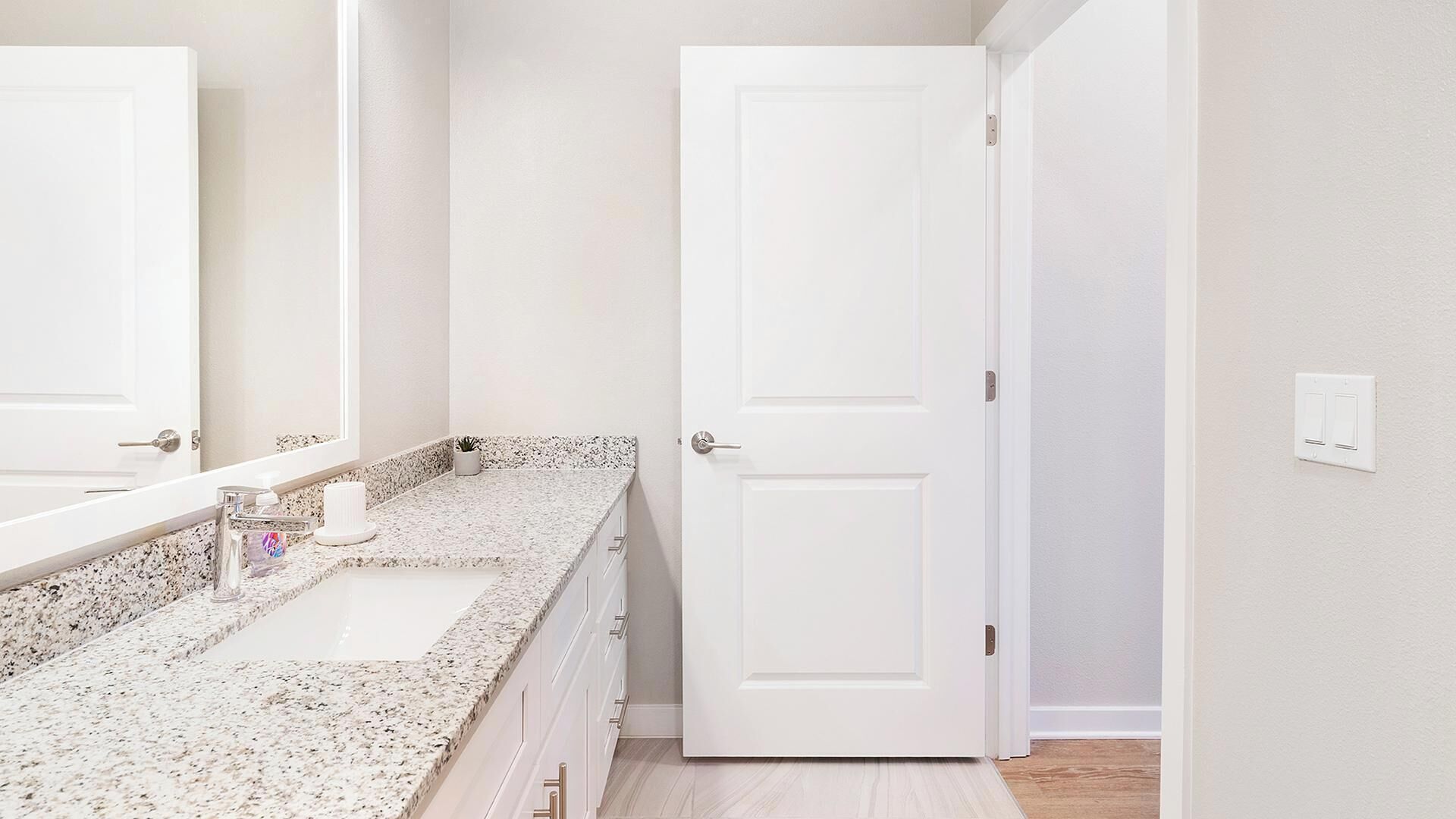 A bathroom with a granite countertop, a white sink, a mirror, and a white door.