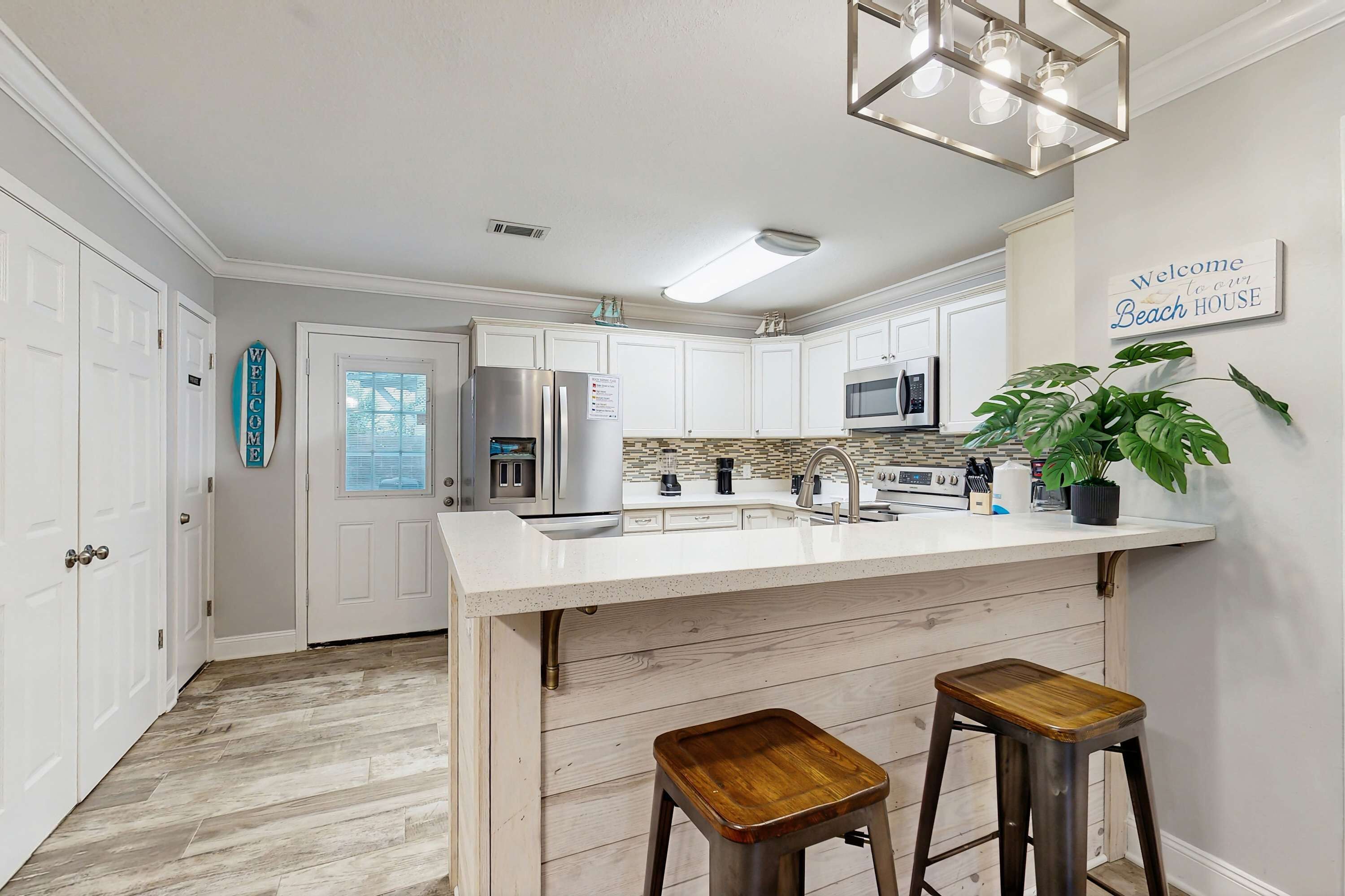A kitchen with white cabinets, a large island, stainless steel appliances, and a 'Welcome to Beach House' sign.