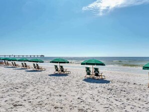 Ein Strand mit Reihen aus grünen Sonnenschirmen und Liegestühlen.