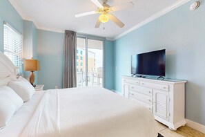 Une chambre d’hôtel avec un lit, un téléviseur posé sur une commode, un ventilateur de plafond et une vue sur l’extérieur.