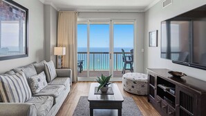 A living room with a sofa, a coffee table, a TV, and a balcony with a view of the ocean. - 25th-floor, waterfront condo with picturesque views, pools & fitness room (Panama City Beach)