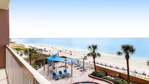 A balcony with a view of a beach and a pool area with sun loungers and umbrellas. - Beach-chic, 7th-floor condo with incredible Gulf-front views, gym, hot tub & 2 pools (Panama City Beach)