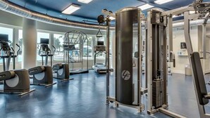 Ein Fitnessstudio mit unterschiedlichen Trainingsgeräten, darunter Laufbänder und Kraftgeräte, und großen Fenstern für natürliches Licht.
