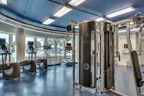 Ein Fitnessstudio mit unterschiedlichen Trainingsgeräten, darunter Laufbänder und Kraftgeräte, und großen Fenstern für natürliches Licht.
