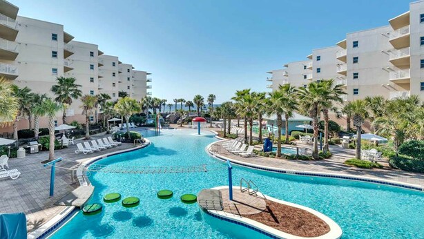 Ein Pool mit Liegestühlen und Palmen, umgeben von mehrstöckigen Gebäuden.