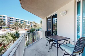 Een balkon met een tafel, stoelen, een plafondventilator en uitzicht op palmbomen en gebouwen.
