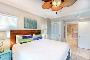 Een slaapkamer met een groot bed, een plafondventilator, een schilderij aan de muur en een deur naar een andere kamer.