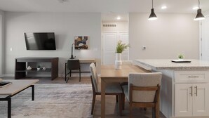 A modern kitchen with a dining area, a TV mounted on the wall, and a small office space. - Landing | Beautiful 2BD, Yoga Studio, Gym (Four Corners)