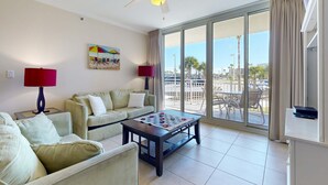A spacious living room with a large window, a ceiling fan, and a foosball table. - Spacious Ground-Floor Condo At Waterscape 490 Feet Of Private Beach (Fort Walton Beach)