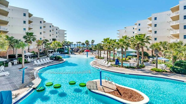 A swimming pool with lounge chairs and palm trees, surrounded by multi-story buildings. - Spacious Ground-Floor Condo At Waterscape 490 Feet Of Private Beach (Fort Walton Beach)