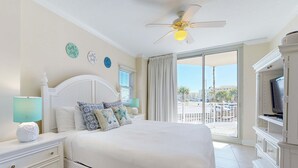 A bedroom with a large bed, a ceiling fan, a TV, and a balcony with a view of palm trees. - Spacious Ground-Floor Condo At Waterscape 490 Feet Of Private Beach (Fort Walton Beach)