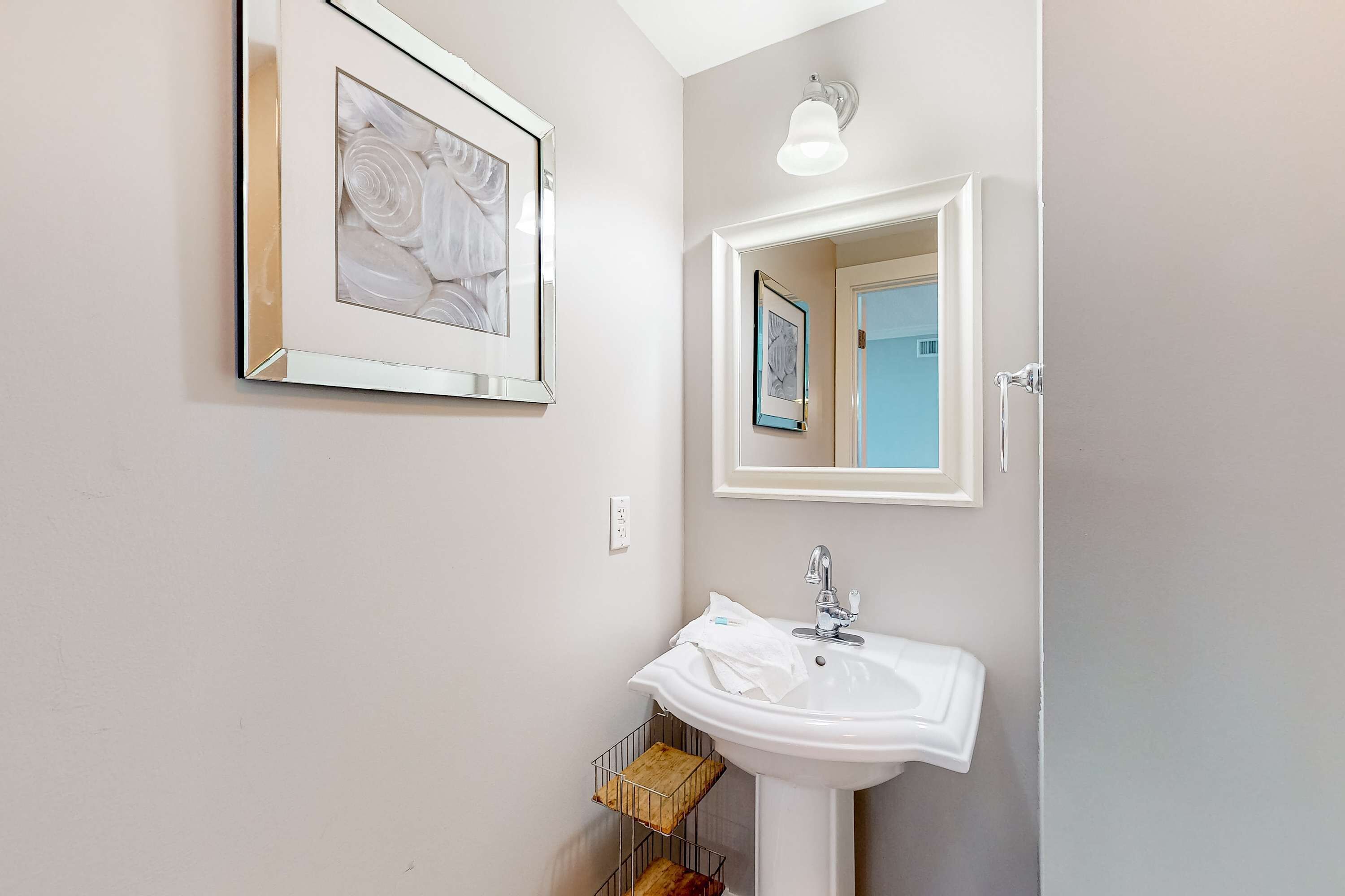 Ein Badezimmer mit einem weißen Waschbecken, einem gerahmten Bild an der Wand und einem Spiegel.
