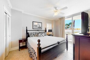 A bedroom with a bed, a nightstand, a ceiling fan, a window with curtains, and a view of palm trees. - Newly renovated, 1st-floor condo with seasonal beach service & beach views (Fort Walton Beach)