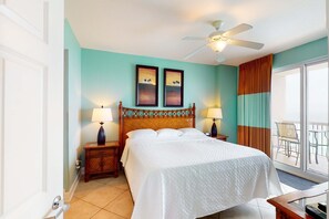 Habitación de hotel con cama, dos lámparas de pared, ventilador de techo y vistas al balcón exterior.