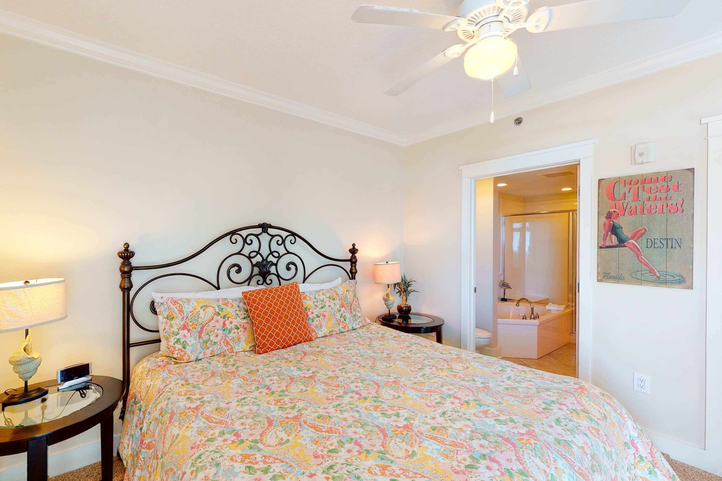A bedroom with a bed, a nightstand, a lamp, a ceiling fan, and a bathroom door.