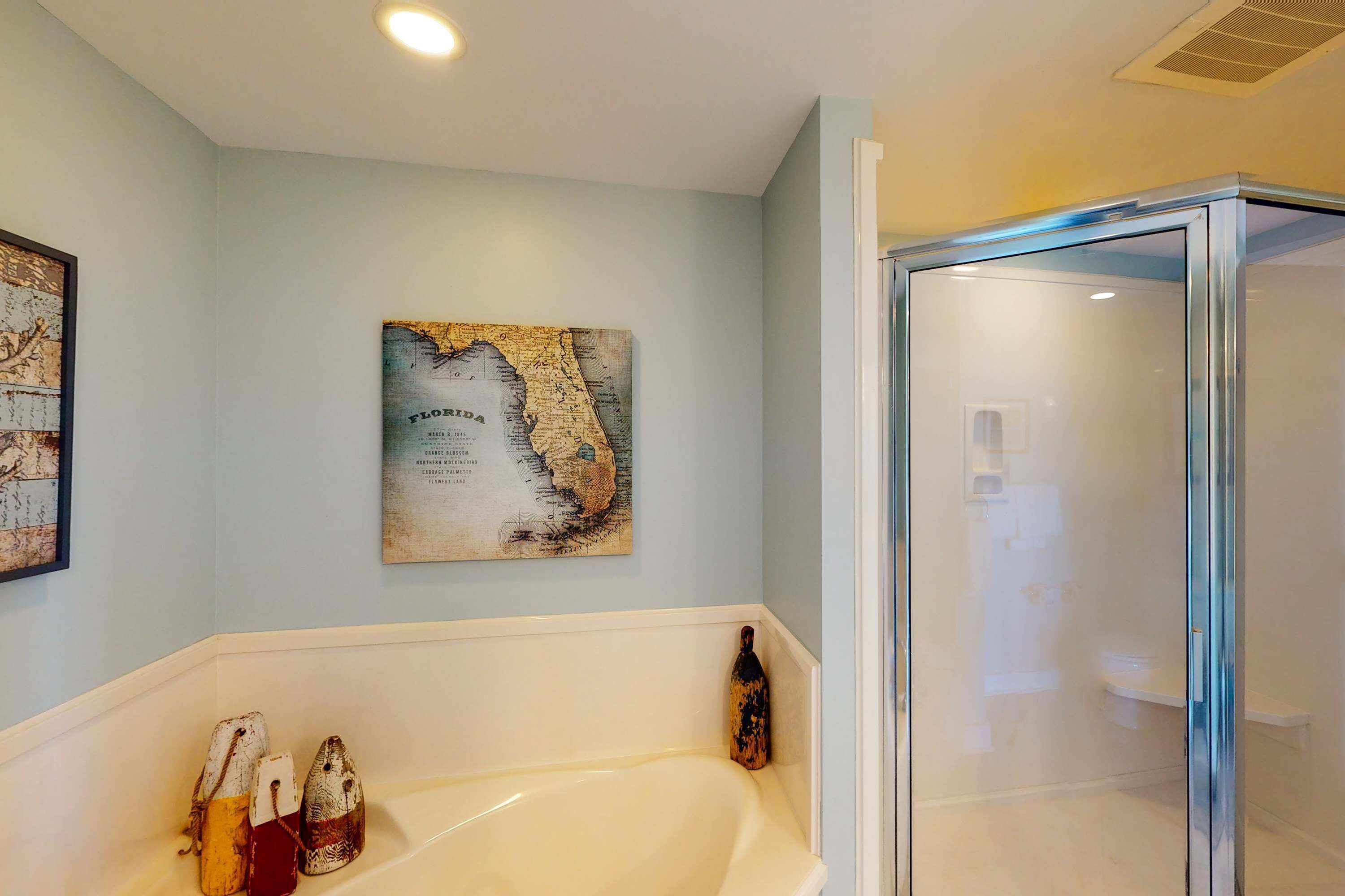 A bathroom with a bathtub, a glass shower enclosure, and a map on the wall.