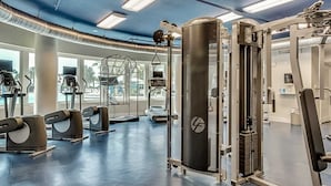 Ein modernes Fitnessstudio mit verschiedenen Trainingsgeräten, großen Fenstern und einer blauen Decke.