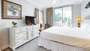 Habitación de hotel con cama, televisión, cómoda, ventilador de techo, ventana con cortinas y vistas al balcón.